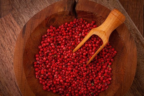 Bright red peppercorns, in a wooden bowl, with a small wooden tray
