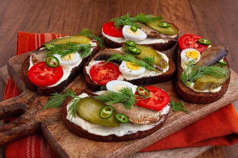 Sandwiches on rye bread with sprats, quail eggs, fresh tomatoes and pickled cucumber, on a wooden