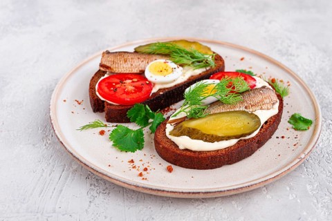 Sandwiches on rye bread, with sprats, quail eggs, fresh tomatoes and pickled cucumber, appetizer,