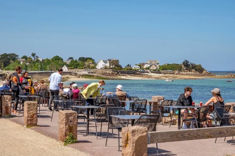 Numerous guests sit at small tables on the sunny terrace of the Grand Hotel Du Port Blanc on the