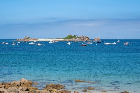 In the turquoise-blue waters of the English Channel, motor boats and sailboats anchor off small,