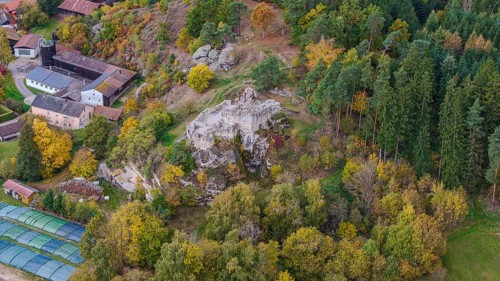 An old castle ruin stands in the middle of the autumn forest, surrounded by colorful trees of