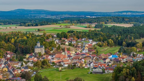 A gentle hilly landscape surrounds a small village with colorful houses and an old castle. The
