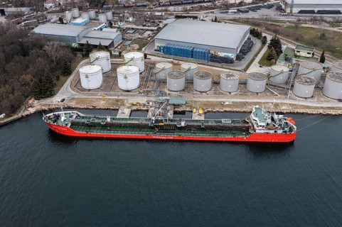 A tanker docked at a port next to large storage tanks
