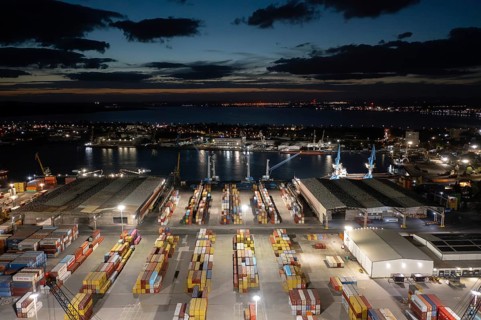 Night view of a bustling port with illuminated containers and cranes by the waterfront. Aerial view