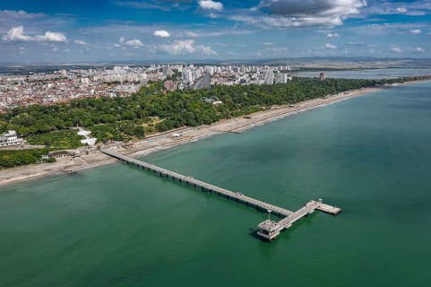 Aerial view of a long pier extending into the sea with cityscape in the background. Aerial view to