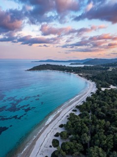 Aerial view of a beach and coastal forest with a peaceful sea at sunset. Aerial view of Glarokavos