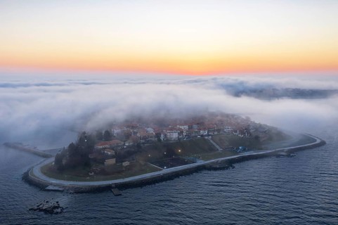 An island surrounded by mist at sunrise with calm waters. Aerial view to thick fog descends over