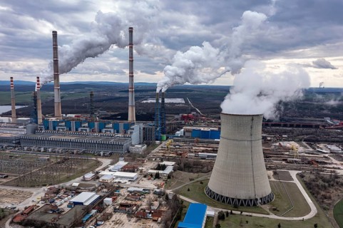 Aerial view of a power plant with multiple smokestacks releasing smoke under a cloudy sky. Aerial