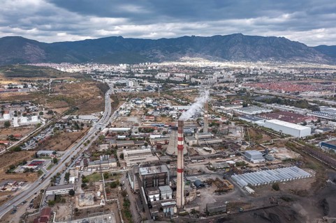 City with industrial facilities and smokestacks nestled among nearby mountains. Aerial view of