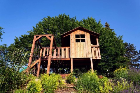 Beautiful wooden children playhouse with swing and slide on hillside Krivoklat Czech republic