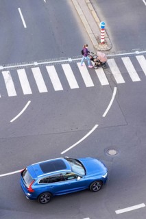 Blue car heading to pedestrian crossing with unrecognizable young woman pushing baby carriage,