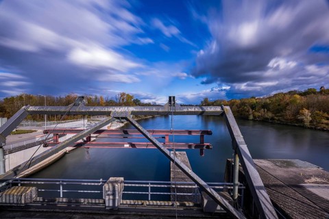 The view shows a lock on a calm body of water. The autumn colors of the trees are reflected in the