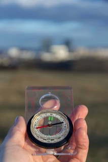 Male hand holding glass compass, nature in background, sunny autumn day, life change and new years