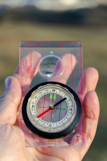 Male hand holding glass compass, nature in background, sunny autumn day, life change and new years