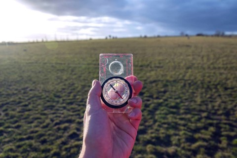Male hand holding glass compass, nature in background, sunny autumn day, life change and new years