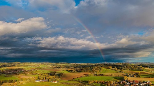 A rainbow stretches across the vast fields and villages. The scene shows vivid colors under a