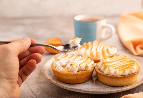 French lemon tart with meringue with hand on brown concrete background, cup of coffee, orange linen