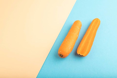 Orange Carrot on orange and blue pastel paper background. Side view, copy space, flat lay. healthy