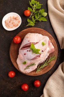 Raw Turkey Thigh with spices and rosemary on cutting board on black concrete background and linen
