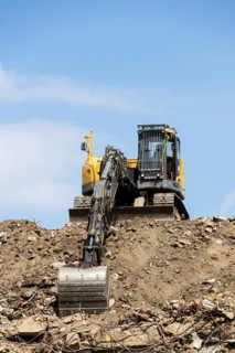 Yellow construction digger, excavator on demolition site stand on debris, sunny day clear blue sky,
