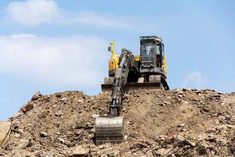 Yellow construction digger, excavator on demolition site stand on debris, sunny day clear blue sky,