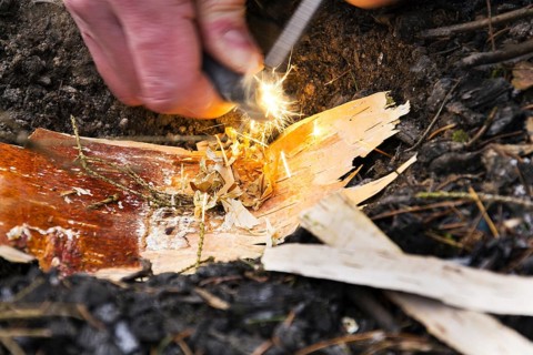Male hand starts fire with magnesium fire steel, fire striker