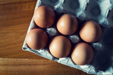Six brown raw hen eggs on gray tray lying on wooden table, copy space