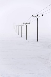 Electricity pylons from distribution power station disappearing in deep fog, winter freezing