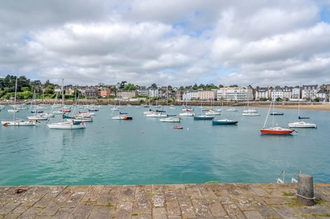 The view from a stone harbor wall shows numerous sailing and motor boats on the turquoise water of