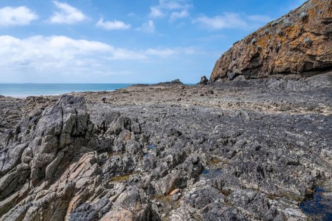 An extensive, humid sandy and rocky beach is exposed in a wide bay at low tide (low tide), with wet