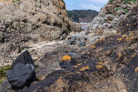 A rugged rock formation, dark and yellow-orange covered with lichens, which forms a narrow opening