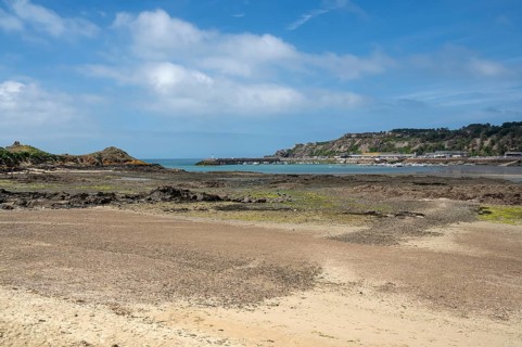 An extensive, humid sandy and rocky beach at low tide stretches out in the foreground, while in the