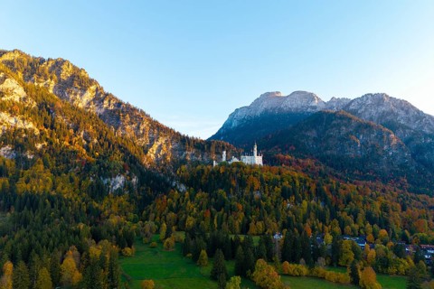 Neuschwanstein Castle perched on a wooded mountain in autumn light with a wide view of the valley,