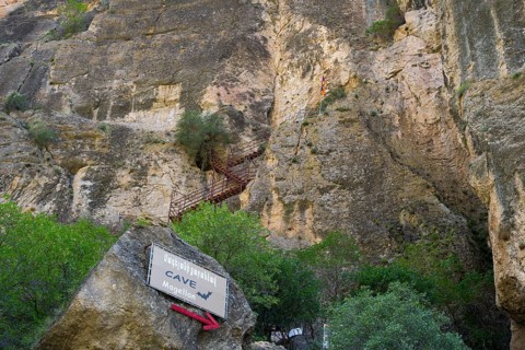 Steep rock wall with a cave and a signpost, Amaghu Gorge, rock wall has a cave with bats to which