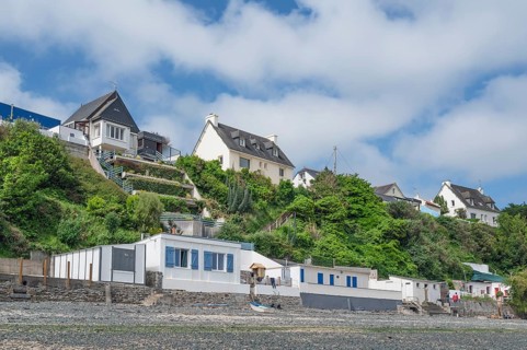 A series of colorful, historic beach cabins with walls of natural stone line the rocky beach at the