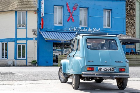 A sky blue Citroën Dyane or 2CV with roll top is parked in front of the bright blue Café Resto du