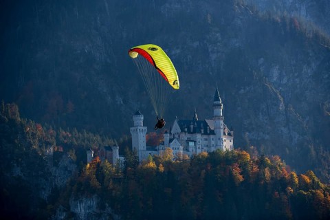 A paraglider flies in front of Neuschwanstein Castle in an autumn landscape, Schwangau, Ostallgäu,