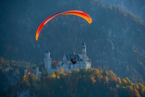 Paraglider flies off Neuschwanstein, nestled in an autumn mountain landscape, Schwangau, Ostallgäu,