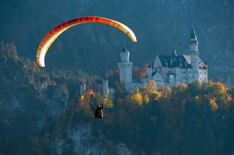 A paraglider floats next to Neuschwanstein Castle in the midst of an autumn landscape, Schwangau,