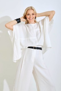A woman stands with her arms raised, showcasing her fashionable white ensemble. She has a bright