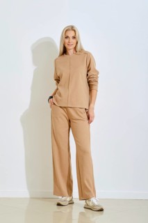 A woman stands confidently in a casual beige outfit featuring a sweater and loose pants. She poses