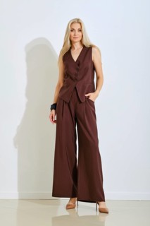 A woman stands elegantly in a chic brown tailored outfit that includes a fitted vest and wide-leg