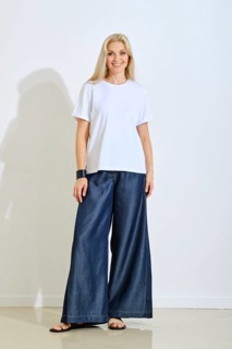 A smiling woman stands confidently in a bright studio space, wearing a simple white t-shirt and