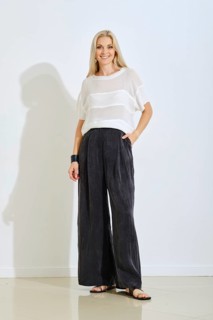 A model stands confidently indoors wearing a light top and loose black pants. The setting features