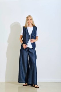 A woman stands confidently in a modern studio dressed in a denim vest and wide-legged pants. The
