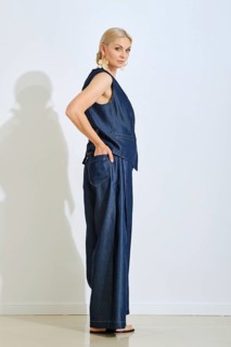 A model stands in profile in a modern studio wearing a sophisticated denim outfit. The light