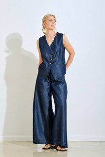 A fashionable woman stands confidently in a sleek denim vest and wide-leg pants. Her accessories