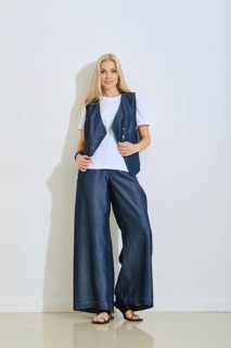 A woman stands confidently in a fashionable outfit consisting of a navy vest over a white shirt and