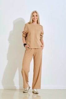 A cheerful woman is posing indoors wearing a light beige two-piece outfit that includes a